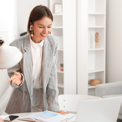Junge Frau im Blazer steht lächelnd an einem Schreibtisch mit offenem Kalender und Laptop – symbolisiert Planung, Motivation und Struktur bei der Lehrstellensuche.
