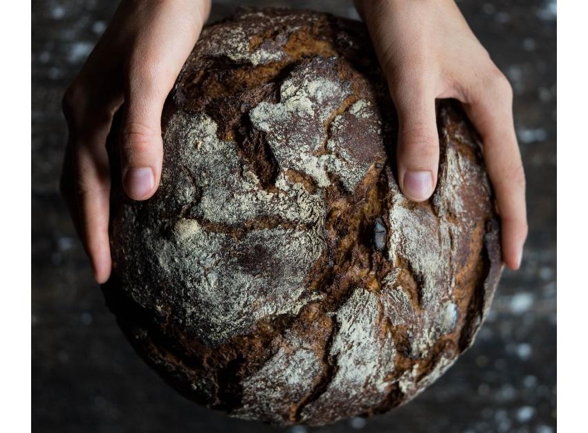 Bäckerlehre: Mit Herz und Hand zum perfekten Brot Zwei Hände halten einen großen, rustikalen Laib Brot – Symbol für traditionelles Bäckerhandwerk.